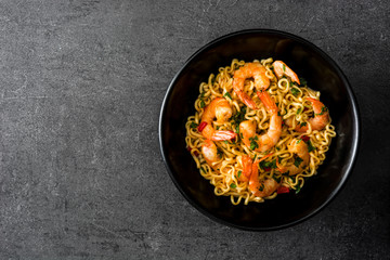 Fototapeta na wymiar Noodles and shrimps with vegetables in black bowl on black stone