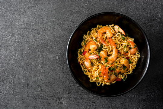 Noodles and shrimps with vegetables in black bowl on black stone

