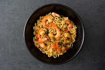 Noodles and shrimps with vegetables in black bowl on black stone

