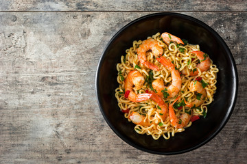 Noodles and shrimps with vegetables in black bowl on wooden table

