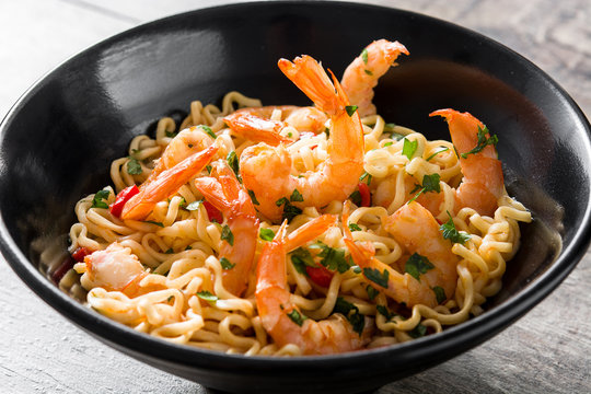 Noodles and shrimps with vegetables in black bowl on wooden table

