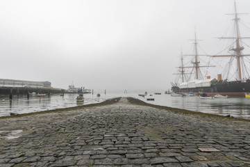 Cobbled Road to the sea with a foggy view of pier and old historic ship