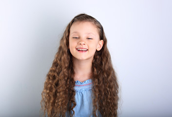 Beautiful natural expression laughing kid girl looking with long curly hair style on blue background