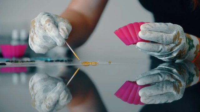 Confectioner makes figure with caramelized sugar on table in kitchen. She puts on glass surface of desk brown liquid sugar in form of figurine for decorating ready-made confectionery boil caramel