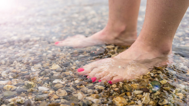 Füße mit pinken Fußnägeln im flachen Wasser