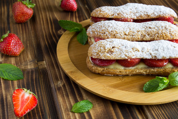 Eclairs with strawberry on the wooden background