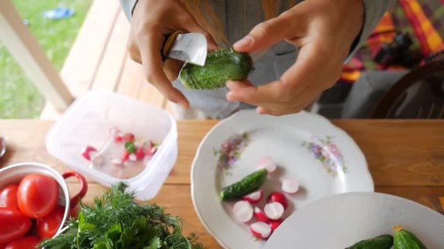 Young woman cutting cucumber for salad on a wooden table. HD slowmotion