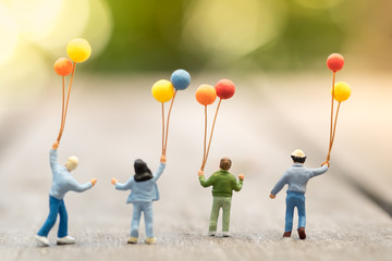 Family and kid concept. Group of children miniature figure with colorful balloons standing, walking and playing together on wooden table. - obrazy, fototapety, plakaty