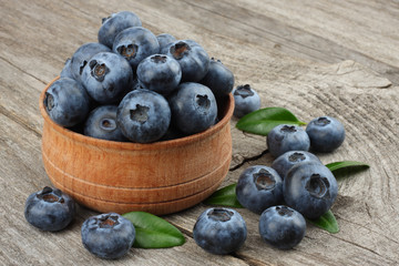 blueberries with green leaf in wooden bowl on old wooden table background