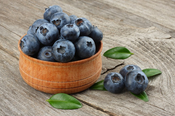 blueberries with green leaf in wooden bowl on old wooden table background