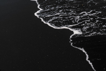weißer ozeanschaum auf schwarzer sandvulkanstruktur
