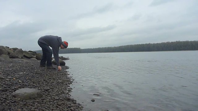 Man walks up to river bank and throws stone that skips.