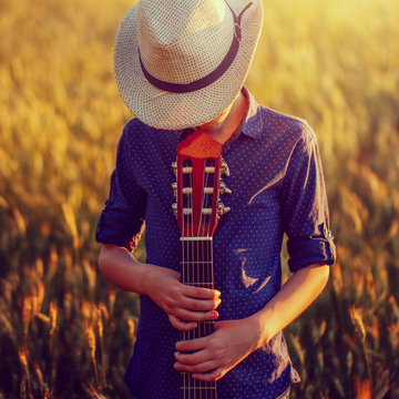 Teenage boy in hat with acoustic guitar, outdoors