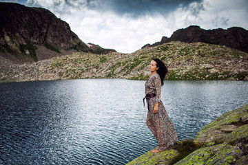 girl in colorful dress on the shore of a clear mountain lake under the storm sky