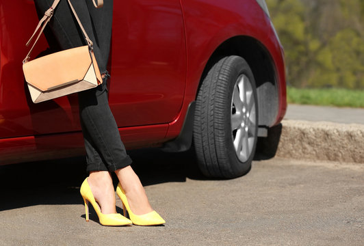 Young woman with slim legs in high heels near car