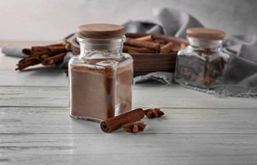 Glass jar with powdered cinnamon, stick and anise on wooden table
