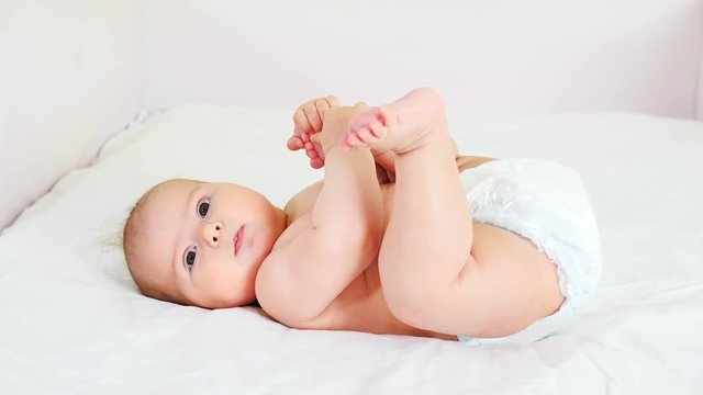 Happy baby in diapers lying on bed