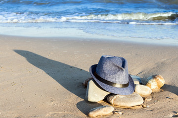 A forgotten male hat with a long shadow on the rocks on the seashore.