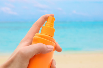 Female hand with bottle of sunscreen cream and blurred sea beach on background. Summer vacation concept