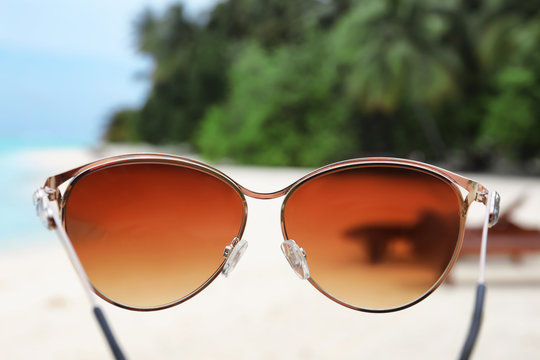 Modern sunglasses and blurred tropical beach on background. Summer vacation concept