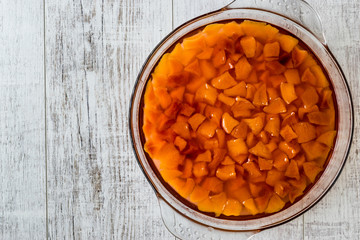 Peach jam in glass bowl on white wooden surface.
