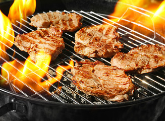 Delicious steaks on grilling grid and flame, closeup