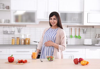 Young pregnant woman standing near table with breakfast in kitchen