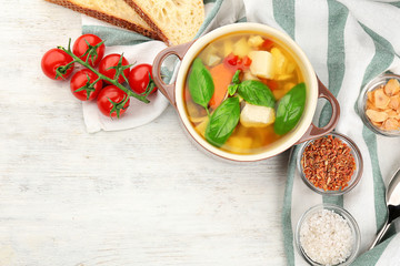 Composition with homemade turkey soup in casserole on light wooden table