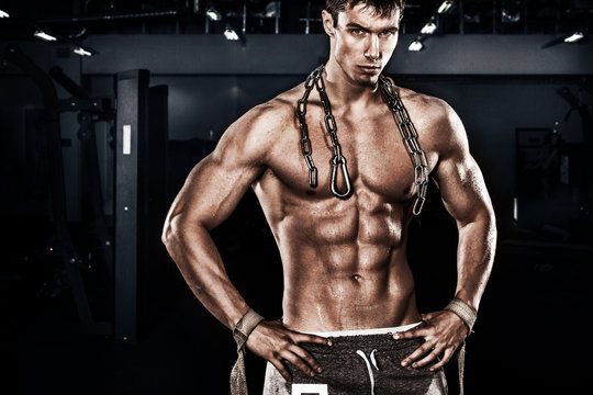 Athletic shirtless young sports man - fitness model holds the chains in gym. Copy space fore your text.