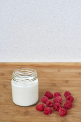 Yogurt in glass jar and raspberries on a wooden background - vertical