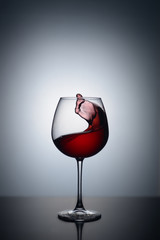 Splash of red wine in a glass on a white background with reflection