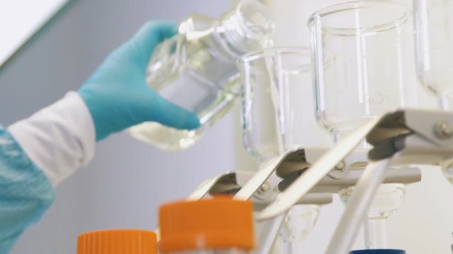 Chemical laboratory: test tubes, flasks, dishes for experiments. Scientists in blue sterile gloves work with chemical utensils and reagents. Laboratory tests in sterile conditions: chemical experiment