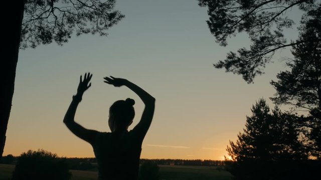Young happy woman dancing and having fun in forest after sunset. Silhouette of woman. Freedom and happiness concept