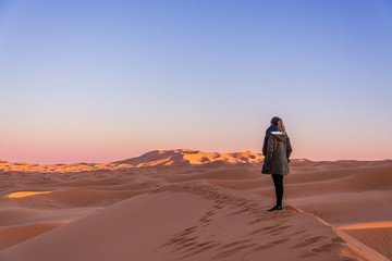 Fototapeta na wymiar Young woman watching sunrise in Sahara desert, Morocco