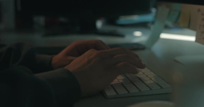 Male hacker working in a dark office. He&rsquo;s a cyber criminal cracking digital security by typing code.