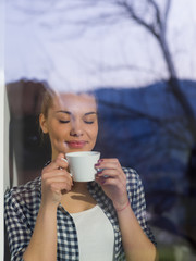 young woman drinking morning coffee by the window