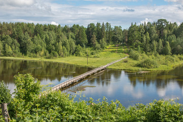 north Russian village Isady. Summer day, Emca river, old cottages on the shore, old wooden bridge and clouds reflections.