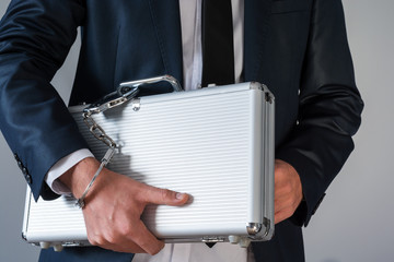 Man in elegant suit holding a suitcase tied with handcuffs to his hand