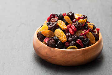 Dried  berries and fruits in wooden bowl on black stone background
