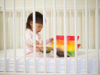 baby girl reading book in cot bed © M-image