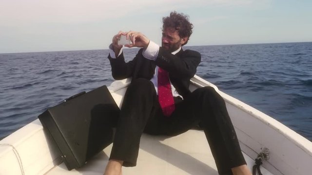 Man in suit with a briefcase taking pictures with his smartphone on a boat in the middle of the ocean