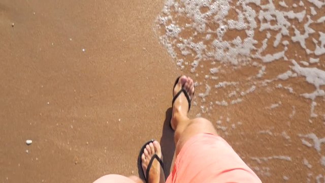 Man Walking in Flip Flops on Sandy Beach into Sea waves. First person view on feet from above. HD Slowmotion.