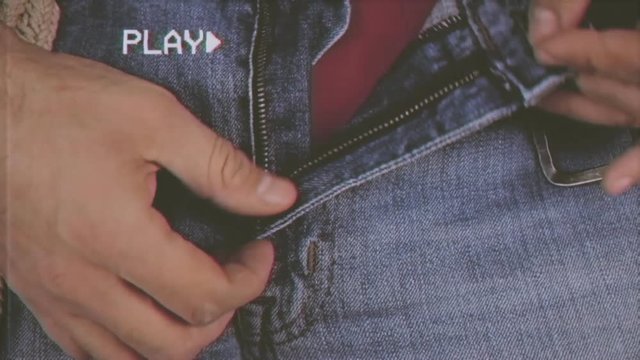 Fake VHS tape: a man opening and closing the zipper of a blue jeans, revealing his red underwear. Close-up detail shot.
