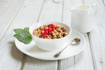 Summer healthy breakfast of granola, muesli with milk jug with red currant decor on light wooden board.