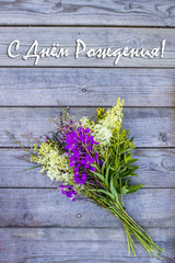 Bouquet of wild summer field flowers on a wooden background. Inscription in Russian "Happy Birthday!"