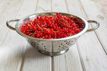 Colander full of freshly harvested red currants on wooden background. Side view.