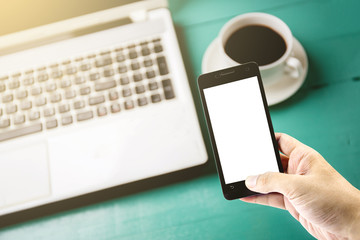 The smartphone in your hand and coffee on the table with laptop