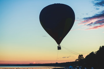 A flying aerostat hot air balloon in flight, with a sun dusk over the beach and blue sky 