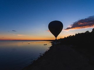 A flying aerostat hot air balloon in flight, with a sun dusk over the beach and blue sky 