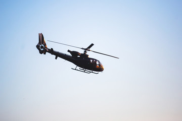 A flying black helicopter aircraft during the flight with blue sky in the background
